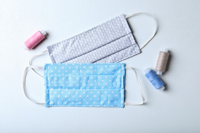 Photo of Homemade protective masks and threads on white background, flat lay. Sewing idea