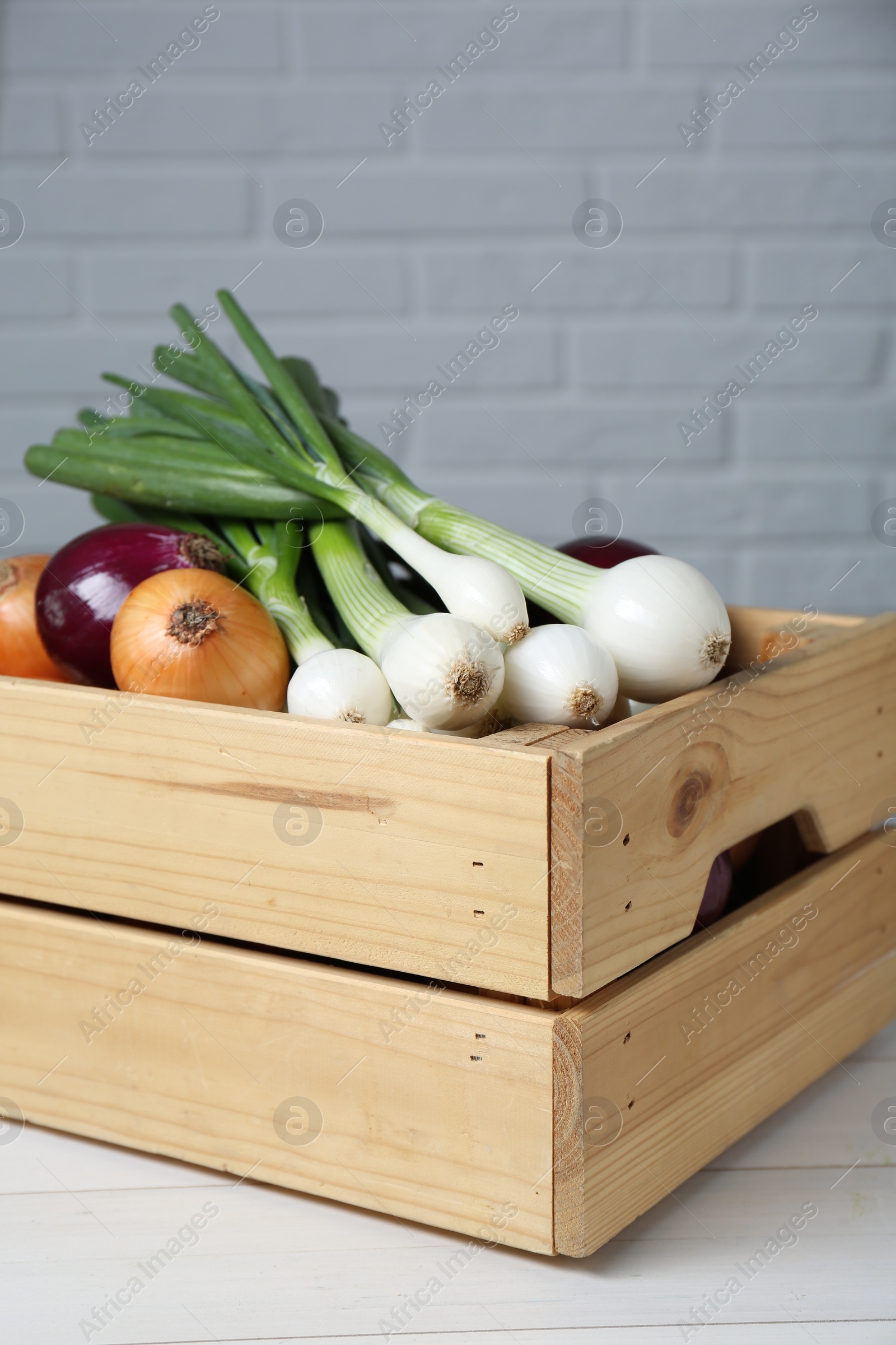 Photo of Crate with different kinds of onions on white wooden table, closeup