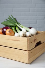 Photo of Crate with different kinds of onions on white wooden table, closeup