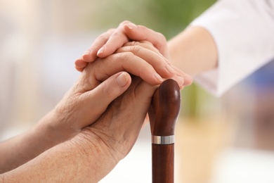 Nurse comforting elderly woman with cane against blurred background, closeup. Assisting senior generation