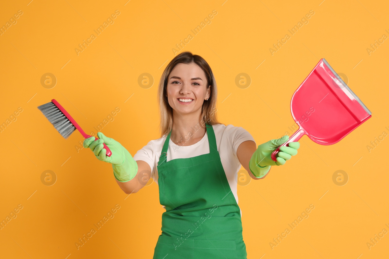 Photo of Young woman with broom and dustpan on orange background