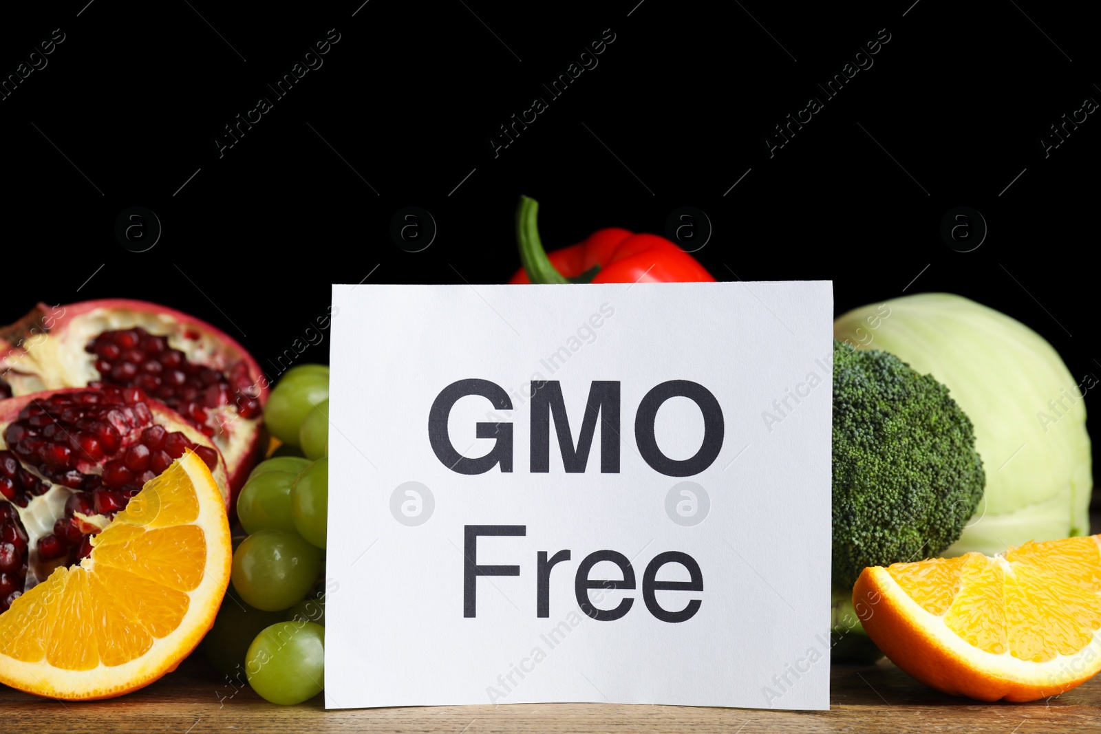 Photo of Tasty fresh GMO free products and paper card on wooden table against black background