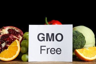 Tasty fresh GMO free products and paper card on wooden table against black background