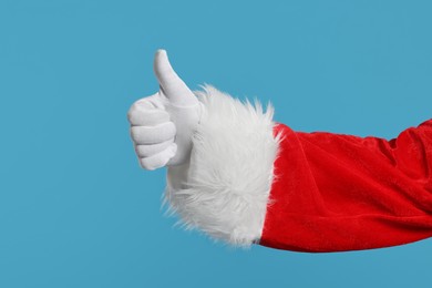 Photo of Merry Christmas. Santa Claus showing thumbs up on light blue background, closeup