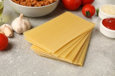 Photo of Cooking lasagna. Pasta sheets and other products on grey textured table