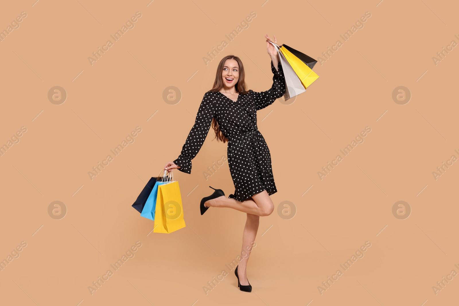 Photo of Stylish young woman with shopping bags on beige background