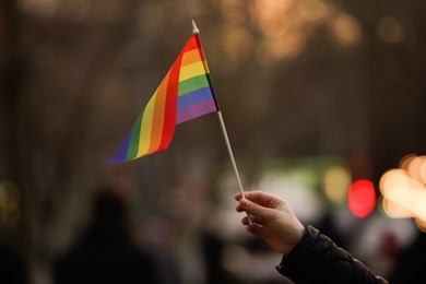 Photo of Woman holding small LGBT flag on city street, closeup