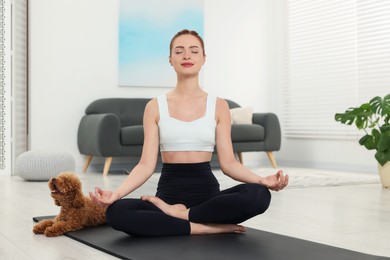 Photo of Young woman practicing yoga on mat with her cute dog at home