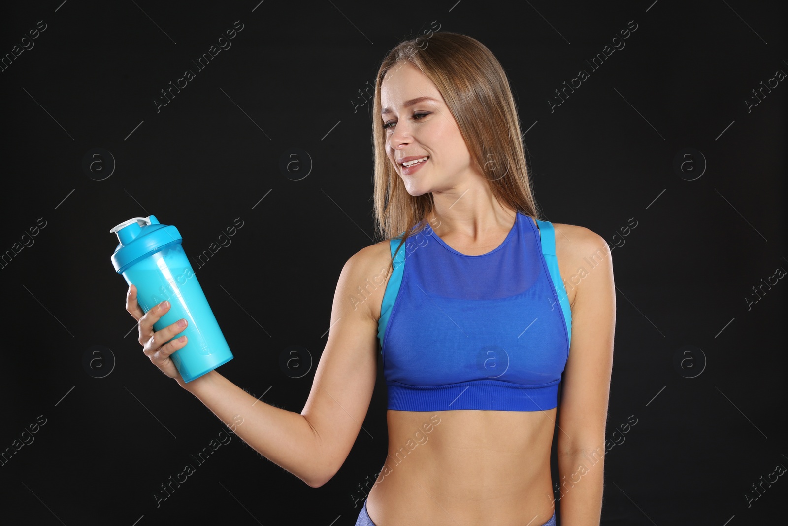 Photo of Portrait of woman with bottle of protein shake on black background