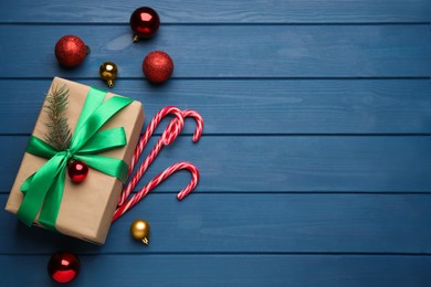 Photo of Tasty candy canes, Christmas balls and gift box on blue wooden table, flat lay. Space for text