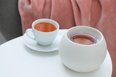 Photo of Wax air freshener and cup of hot tea on white table indoors. Interior element