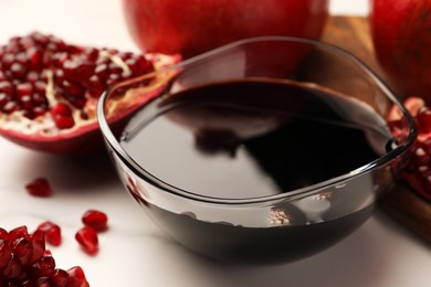 Photo of Glass bowl of tasty pomegranate sauce and fresh ripe fruits on white marble table, closeup