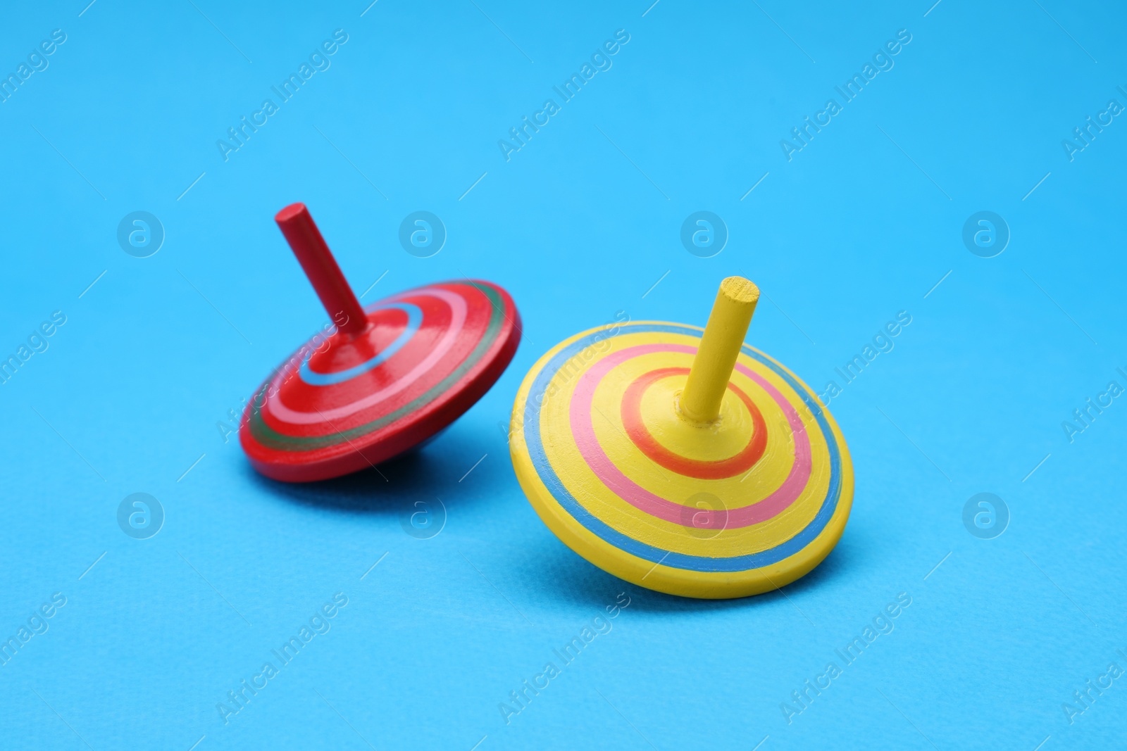 Photo of Two bright spinning tops on light blue background. Toy whirligig