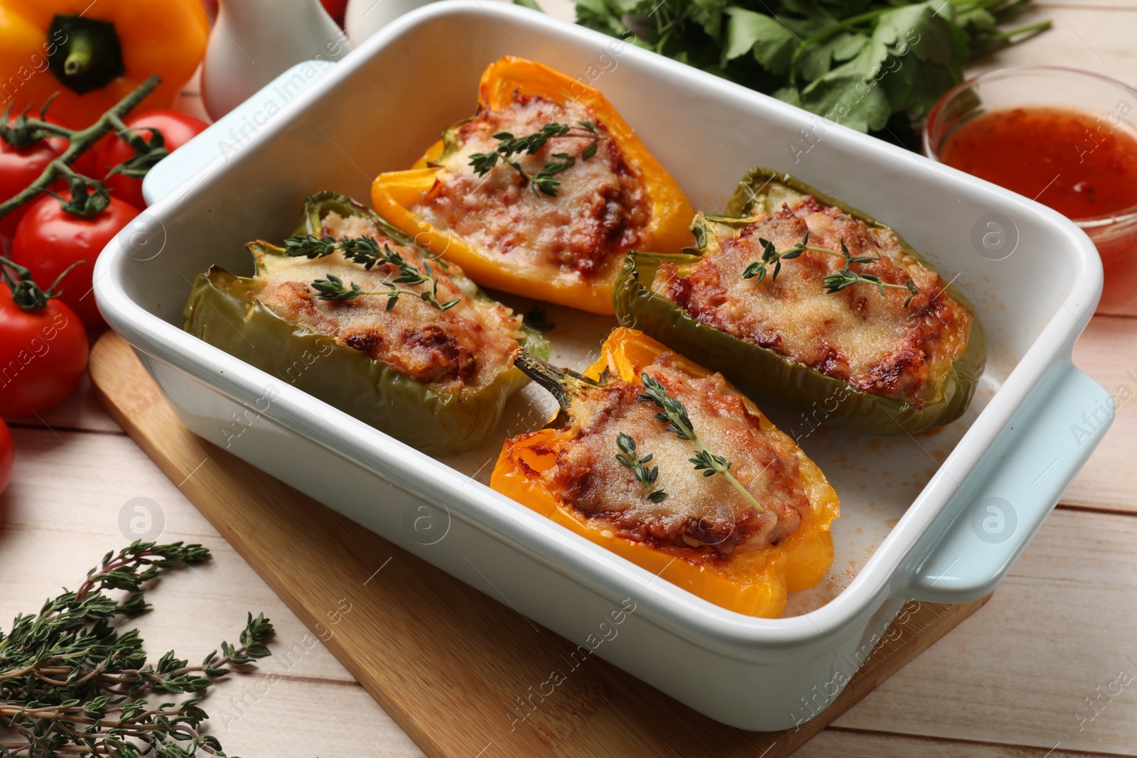 Photo of Tasty stuffed peppers in dish and ingredients on wooden table