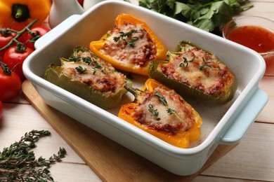 Photo of Tasty stuffed peppers in dish and ingredients on wooden table