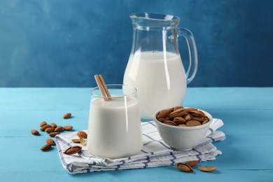 Glass of almond milk, jug and almonds on light blue wooden table