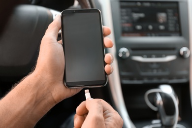 Photo of Man connecting charging cable to smartphone in car, closeup