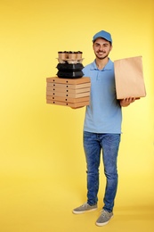 Young courier with different orders on color background. Food delivery service