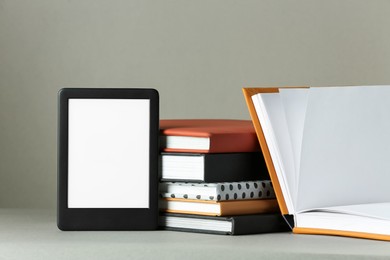 Modern e-book reader and hard cover books on light grey table