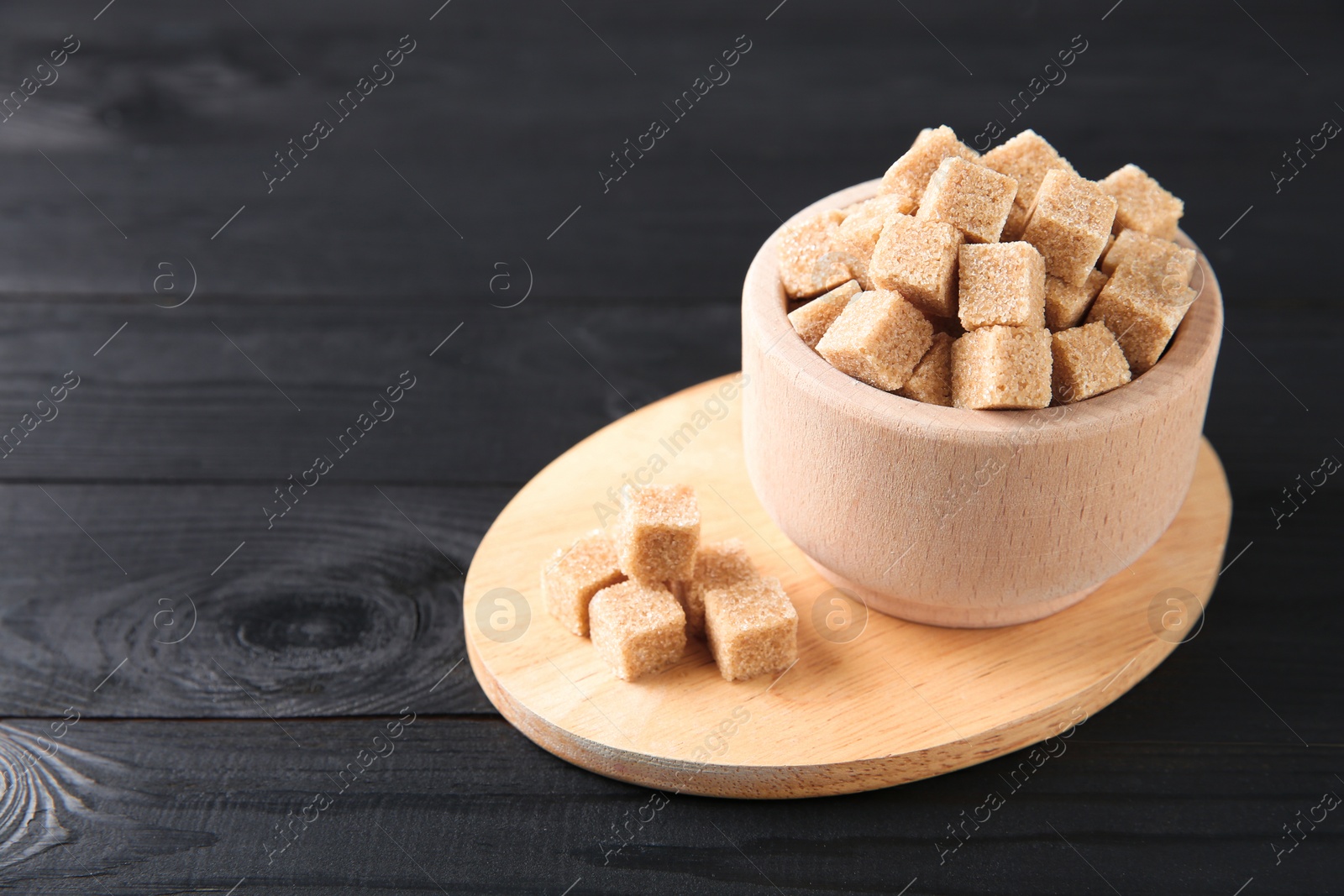 Photo of Brown sugar cubes in bowl on black wooden table. Space for text