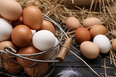 Photo of Fresh chicken eggs and dried straw on black wooden table, closeup