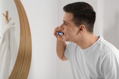 Photo of Man brushing his teeth with electric toothbrush in bathroom