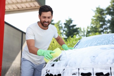 Photo of Happy man washing car with sponge outdoors