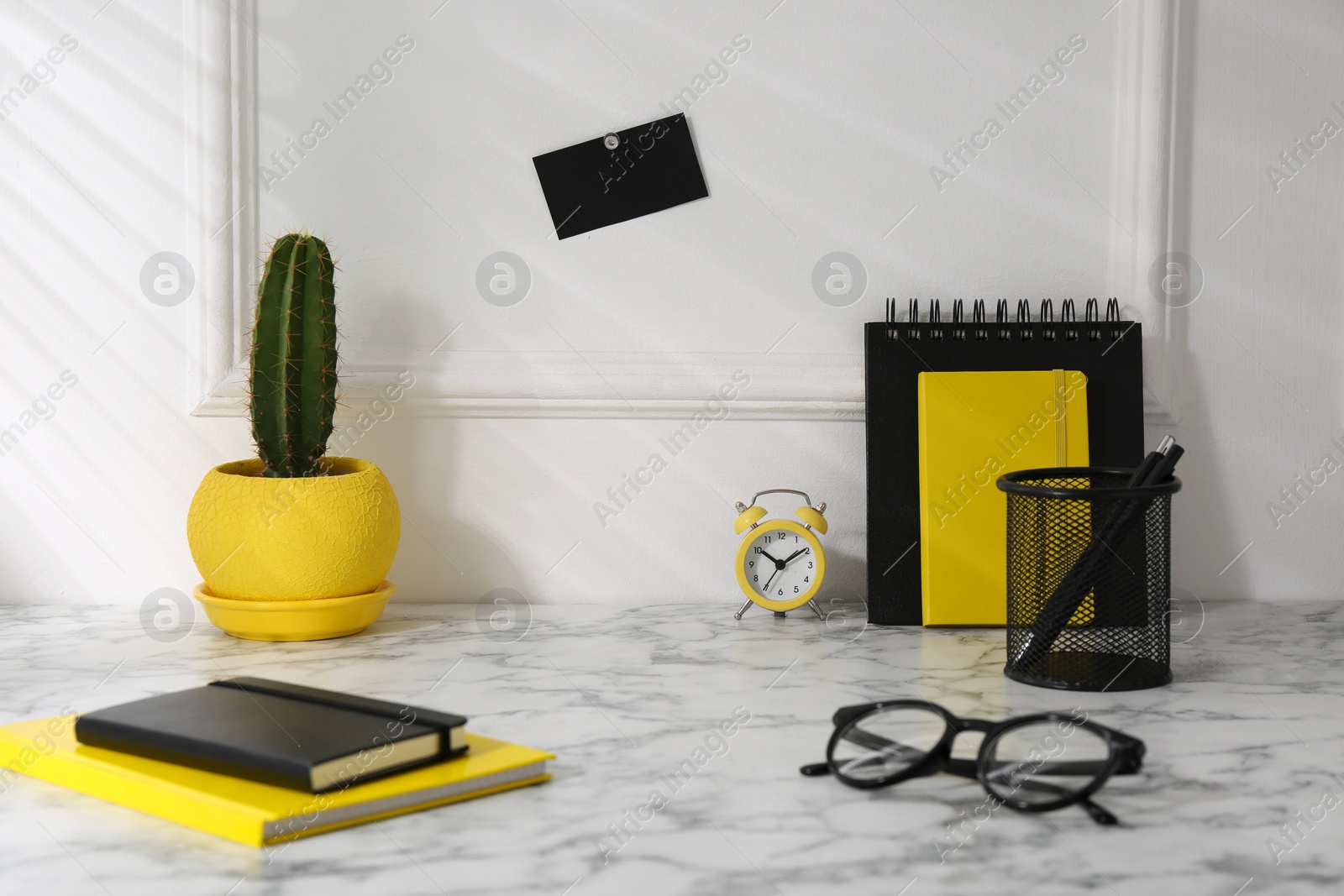 Photo of Stylish office workplace. Decor elements, cactus, glasses and stationery on marble table near white wall