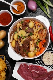 Pot of delicious vegetable soup with meat, noodles and ingredients on black wooden table, flat lay