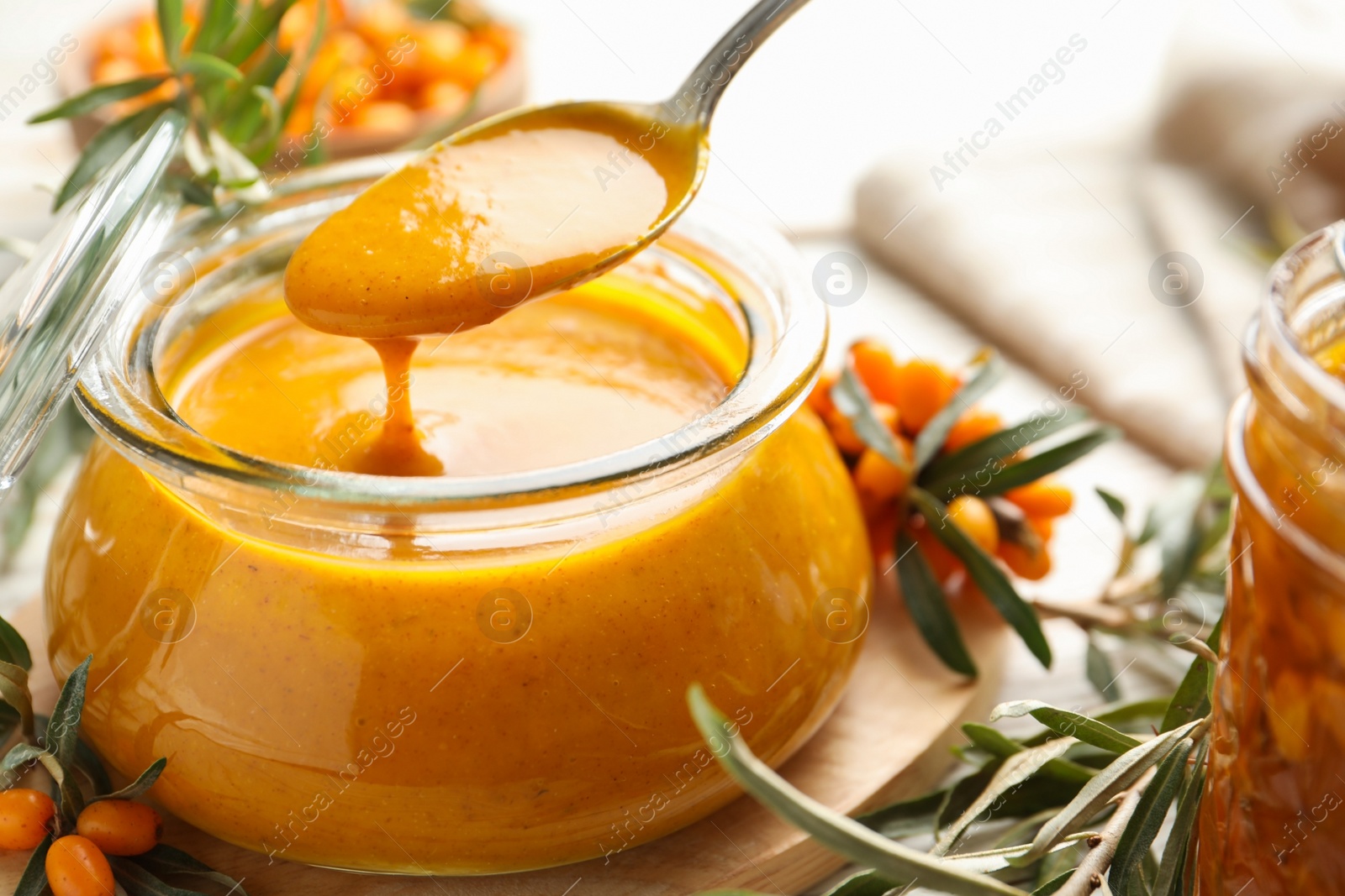 Photo of Spoon with delicious sea buckthorn jam over jar on table, closeup
