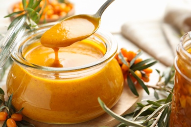 Spoon with delicious sea buckthorn jam over jar on table, closeup