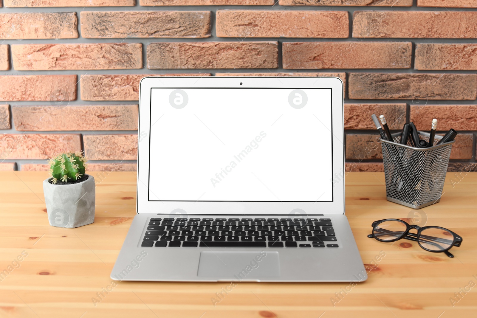 Photo of Modern laptop on table against brick wall. Mock up with space for text