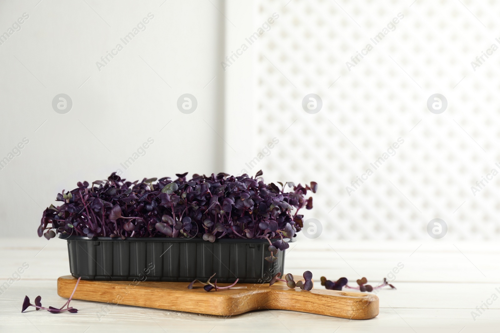 Photo of Fresh radish microgreens in plastic container on white wooden table, space for text