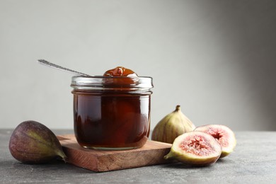 Photo of Jar of tasty sweet jam and fresh figs on grey table. Space for text