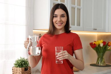 Young woman with jug and glass of water in kitchen