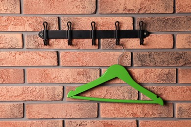 Photo of Hook rack with green clothes hanger on red brick wall. Space for text