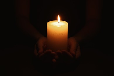 Woman holding burning candle in hands on black background, closeup