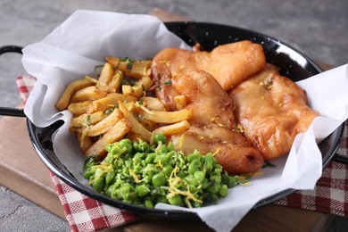 Photo of Tasty fish, chips and peas on grey table, closeup