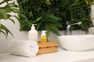 Photo of Green artificial plants, vessel sink and different personal care products in bathroom
