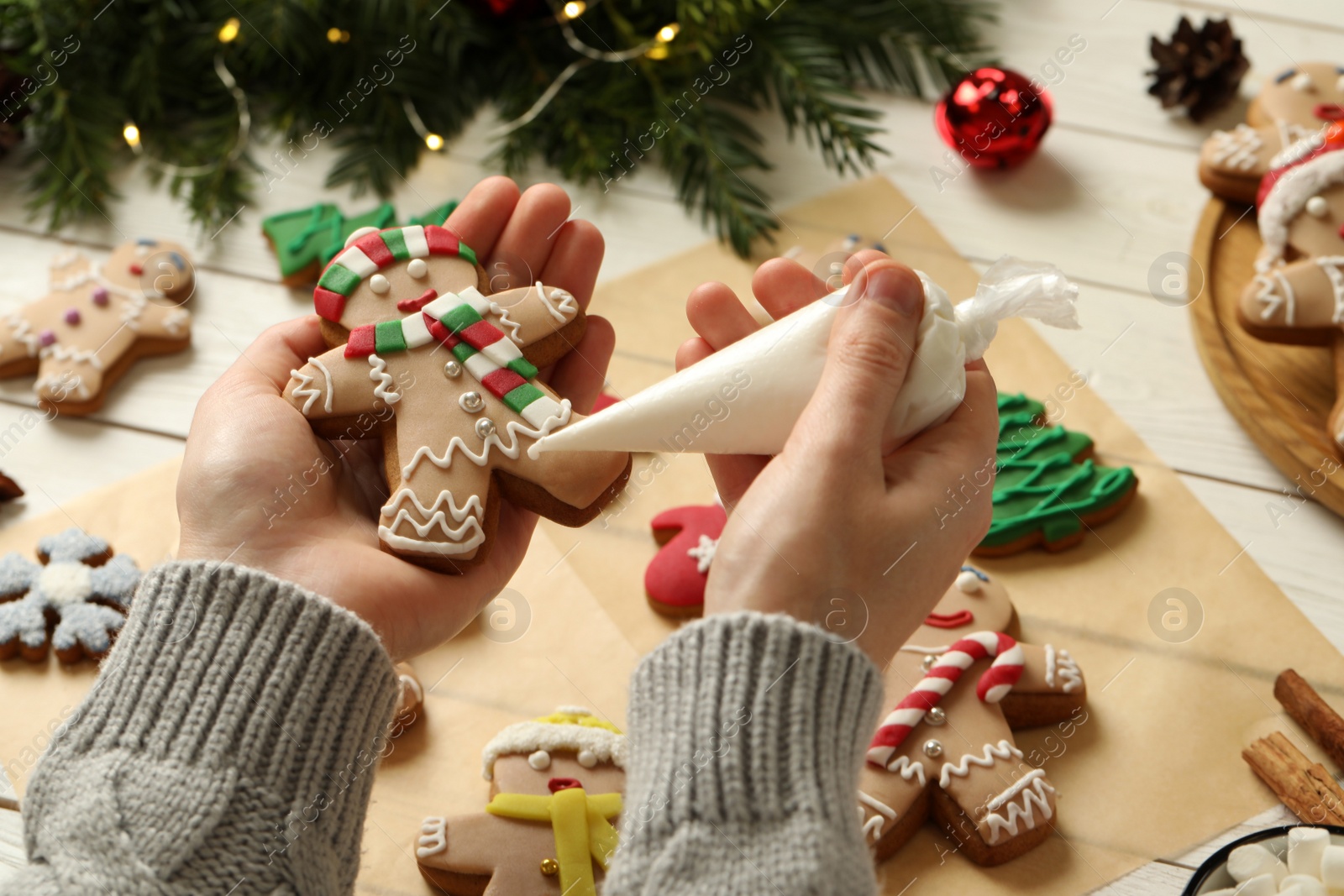 Photo of Making homemade Christmas cookies. Girl decorating gingerbread man at white wooden table, closeup