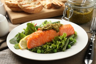 Photo of Tasty cooked salmon with pesto sauce and fresh salad served on wooden table, closeup