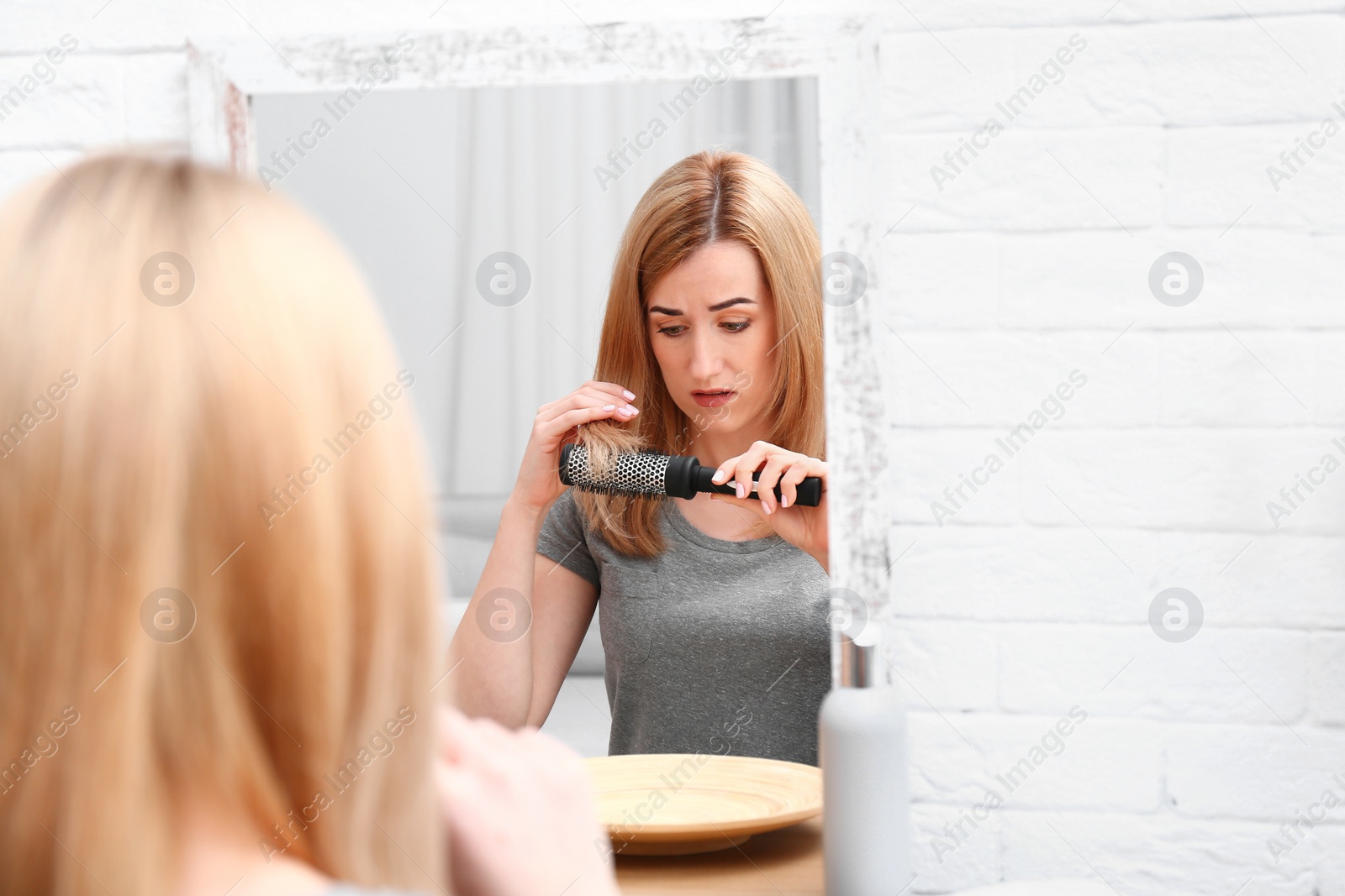 Photo of Emotional woman brushing hair near mirror in bathroom