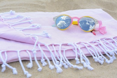 Blanket with stylish sunglasses and flower on sand outdoors, closeup. Beach accessories