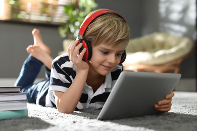 Cute little boy with headphones and tablet listening to audiobook at home