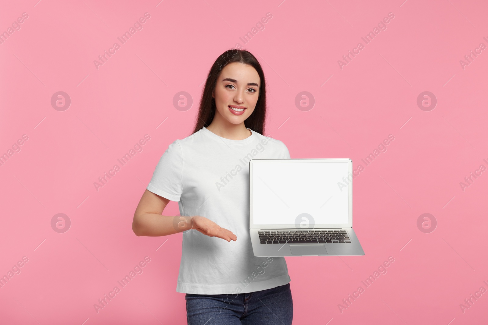 Photo of Smiling young woman showing laptop on pink background