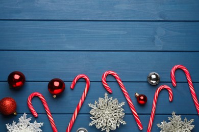 Tasty candy canes, Christmas balls and snowflakes on blue wooden table, flat lay. Space for text
