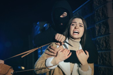 Photo of Criminals threatening young woman with knife outdoors at night. Self defense concept