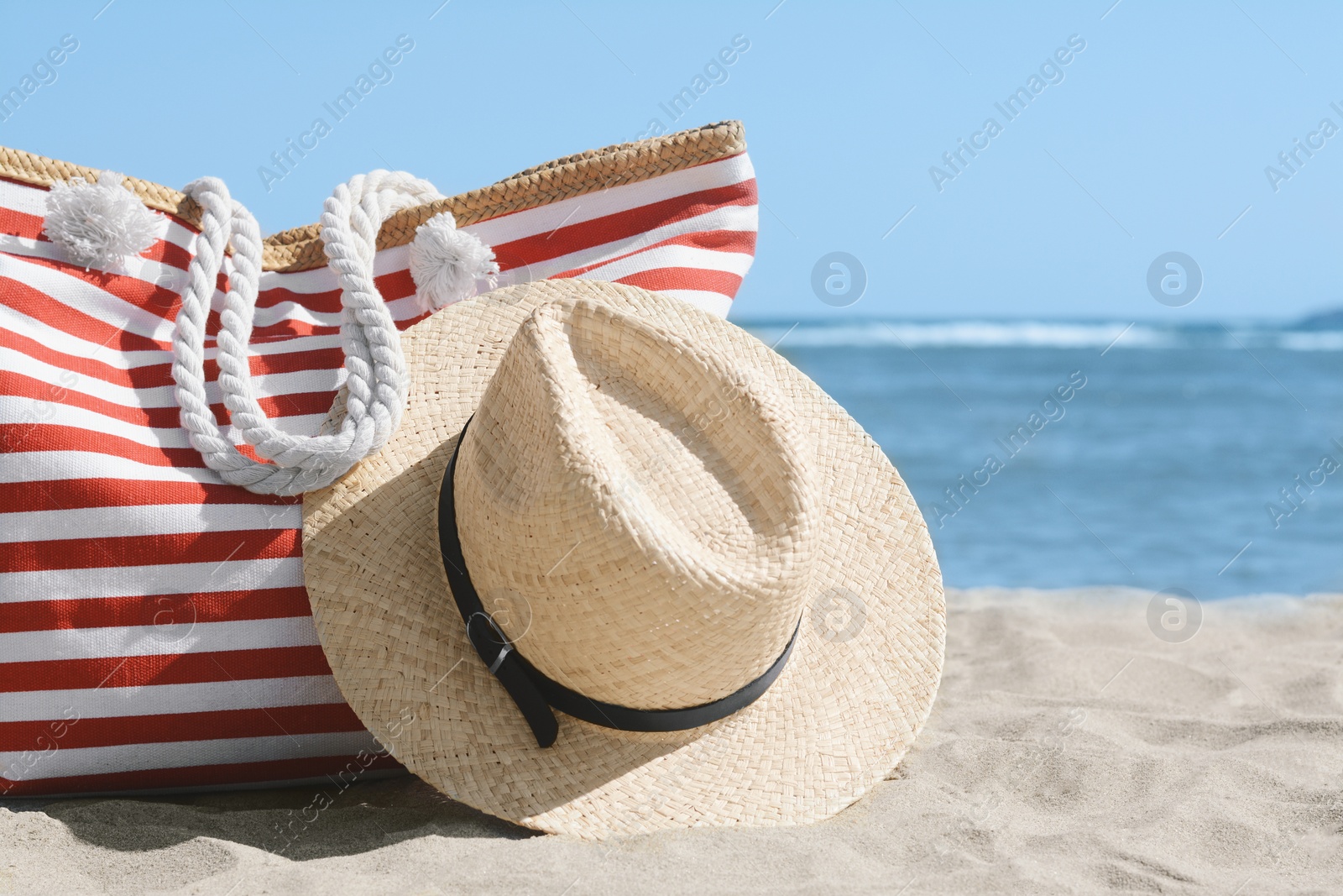 Photo of Stylish striped bag with straw hat on sandy beach near sea