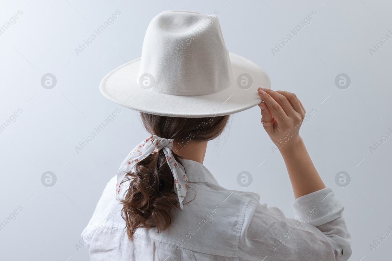 Photo of Young woman with hat and stylish bandana on light background, back view