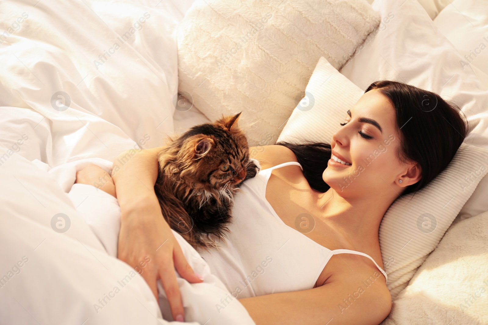 Photo of Beautiful young woman with her cute cat on bed. Fluffy pet